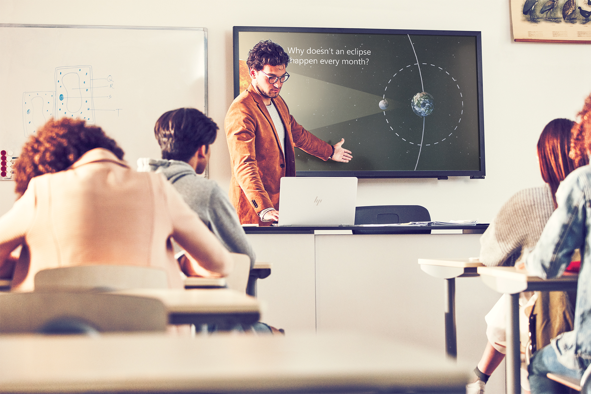 Teacher standing in front of large monitor, teaching classroom of students