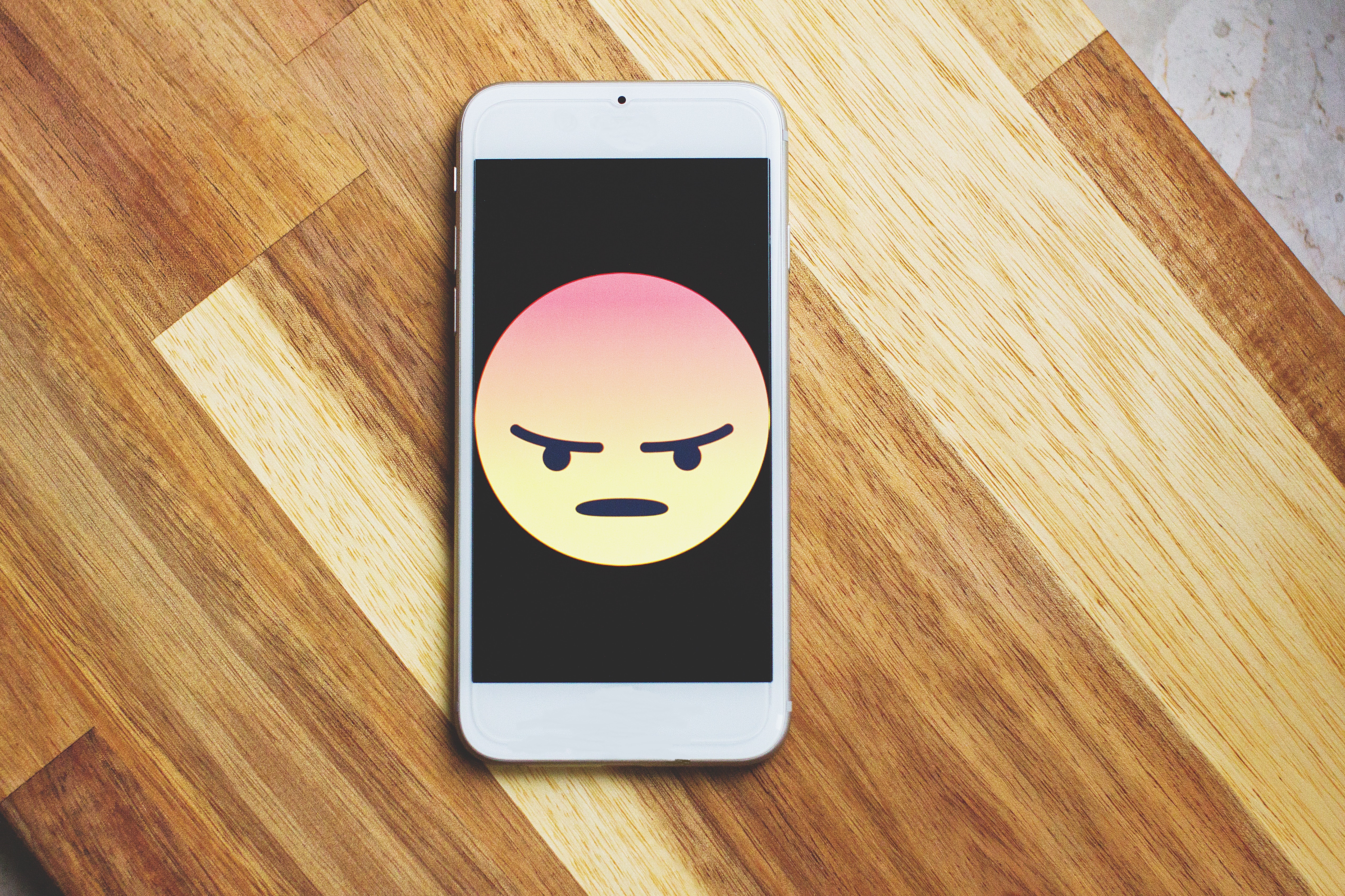 Angry emoji on a mobile phone sitting on a desk