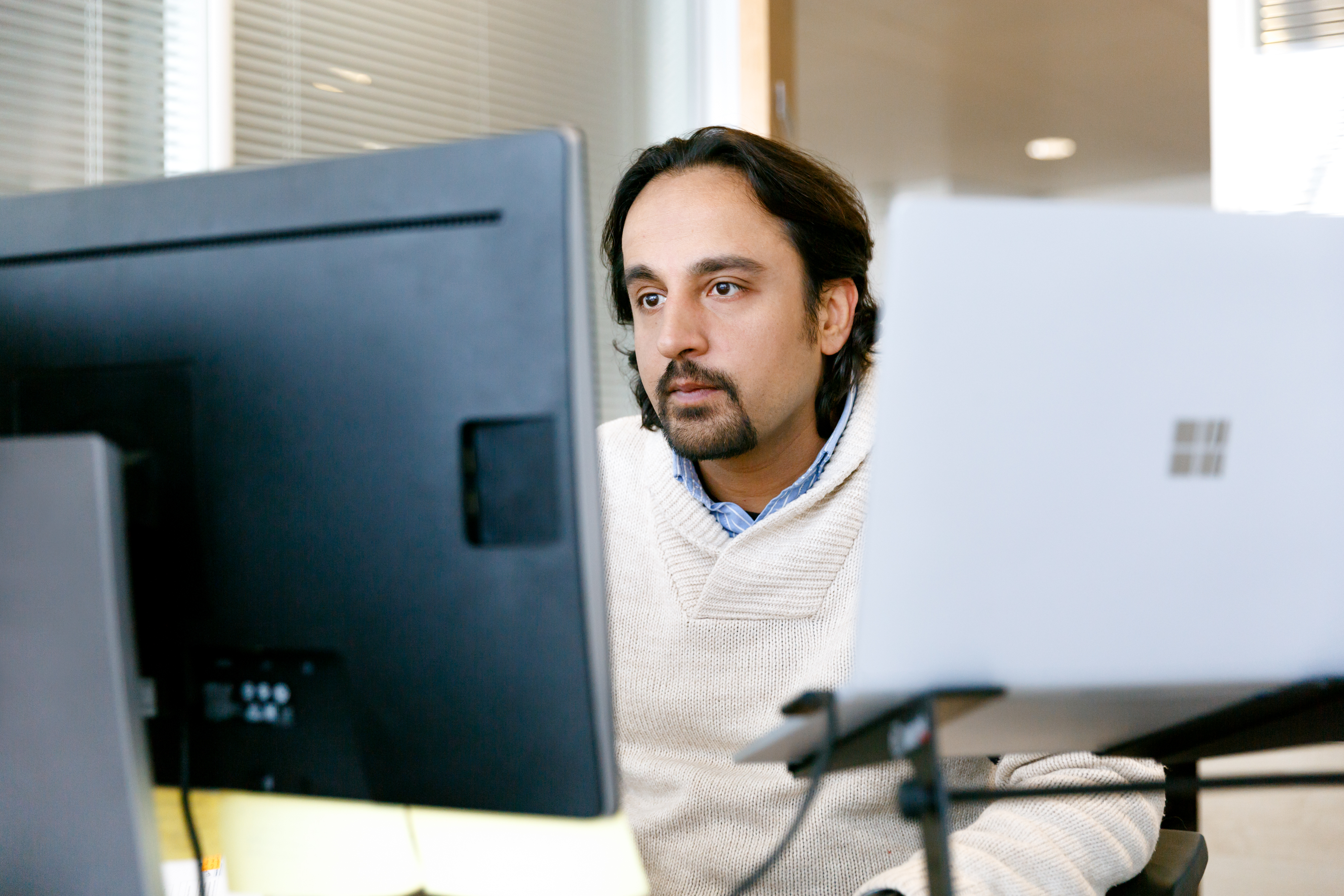 Man at office desk looking at computer monitor, with Surface device next to him