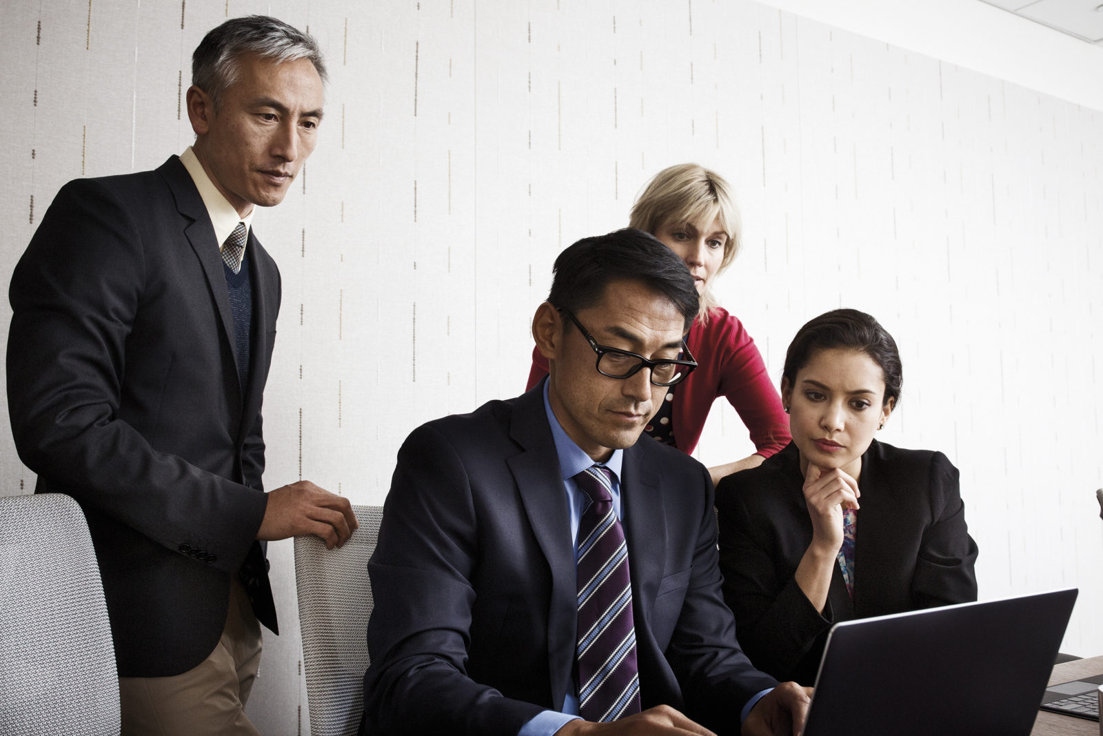 Office staff crowd round a laptop, looking at screen