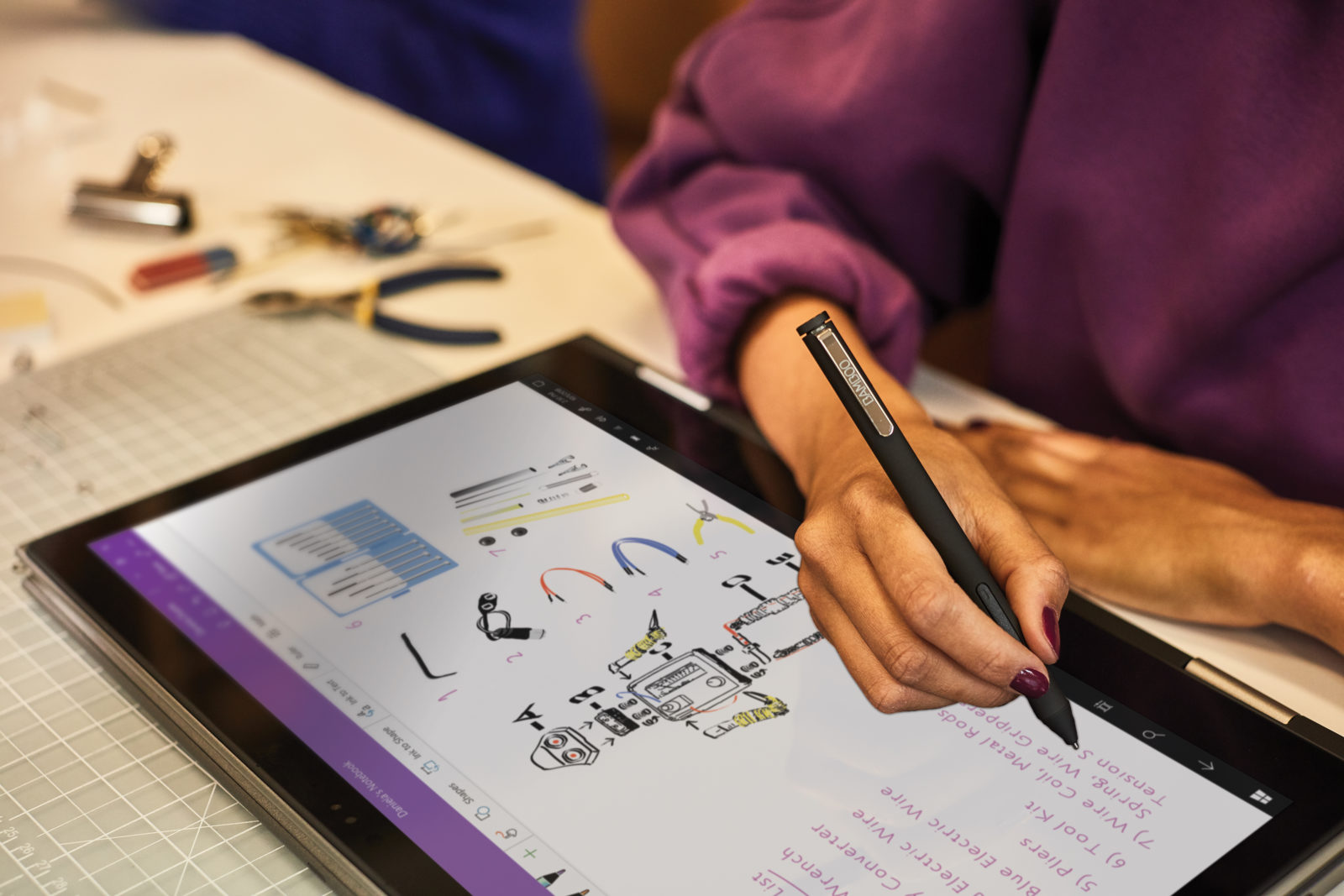 Young person writing on a Microsoft Surface laptop in a classroom