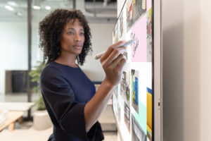 A woman writes on a Surface Hub 2S in an office