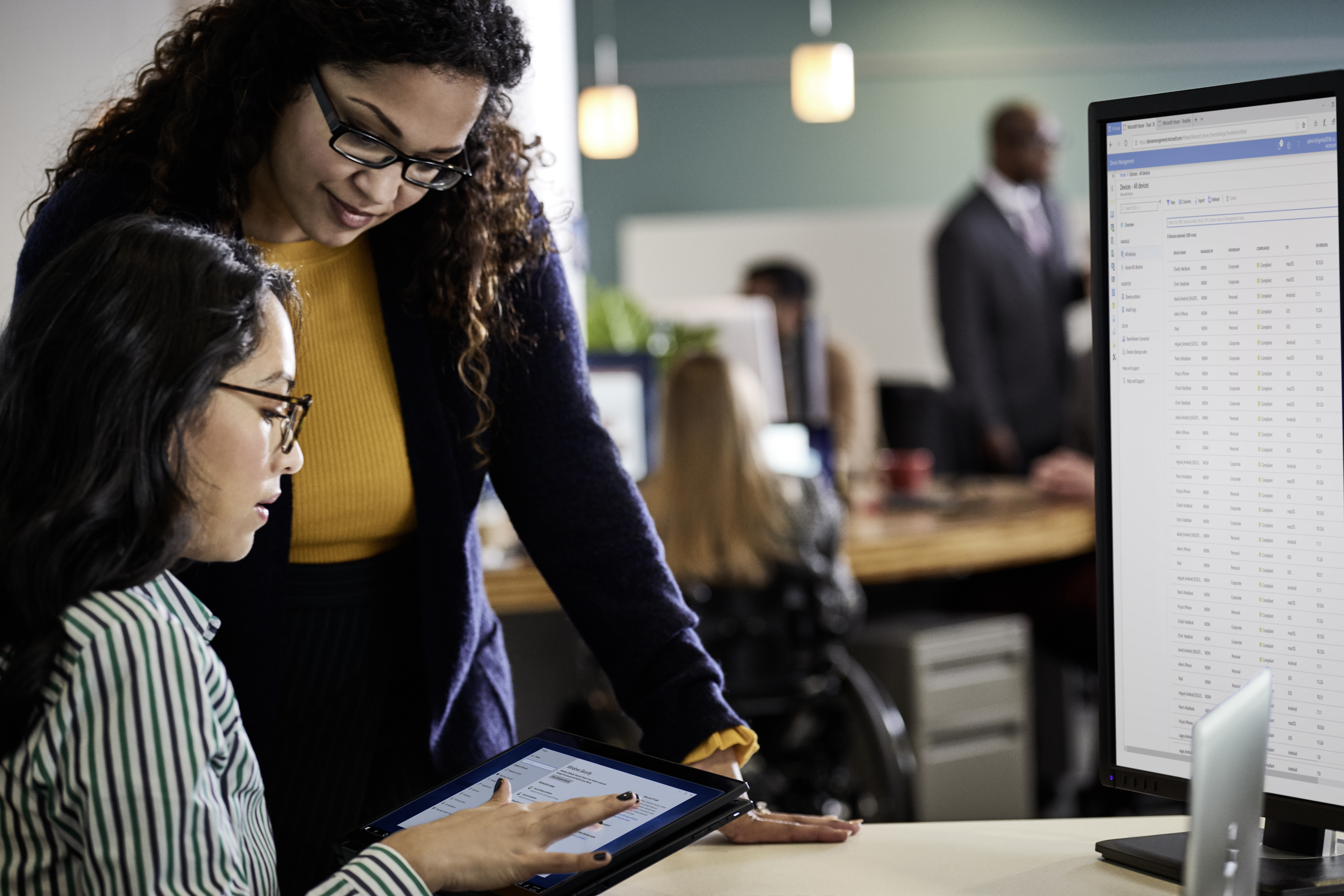 Female enterprise coworkers collaborating in an open office space, working on a HP Elitebook touch screen device.