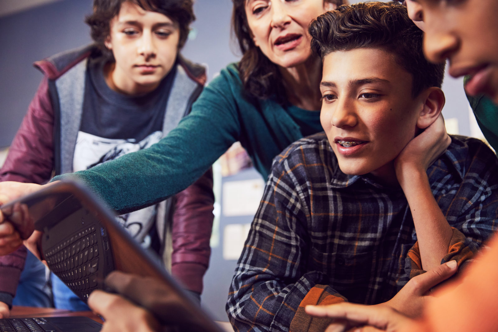 Female teacher shows three students something on a laptop screen