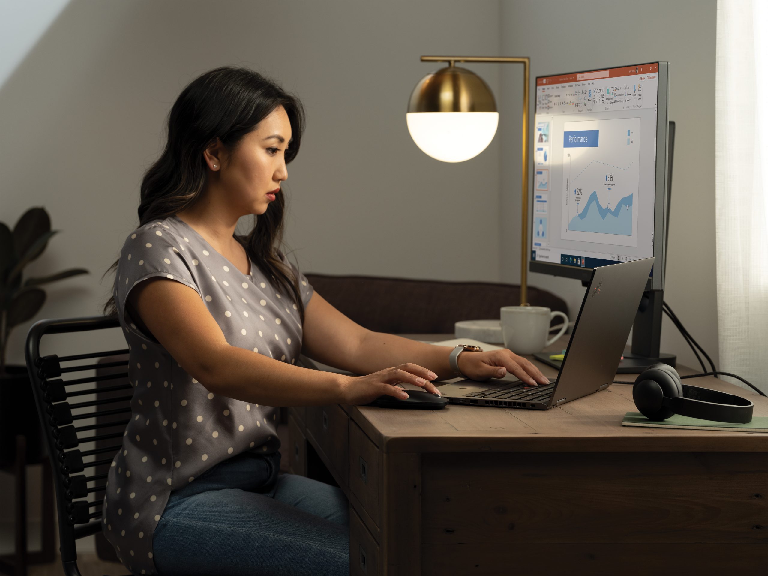 A woman working at her home office on a Lenovo ThinkPad Yoga connected to an external monitor displaying a PowerPoint file