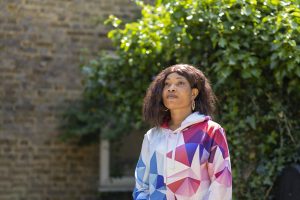 A woman stands against a wall looking away into the distance