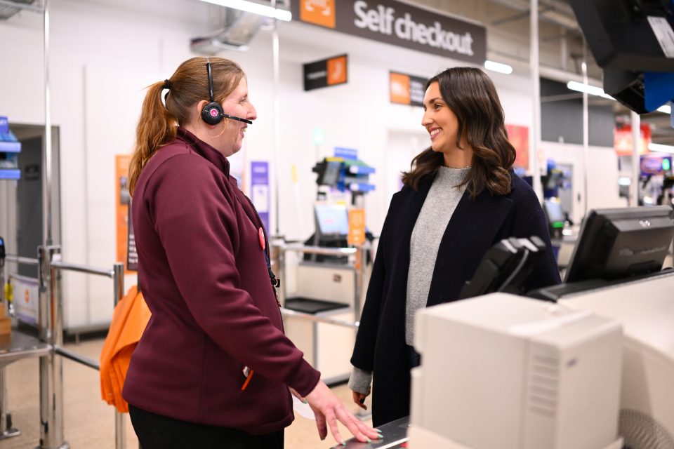 Sainsbury's staff member wearing a headset talking to a young shopper in a store