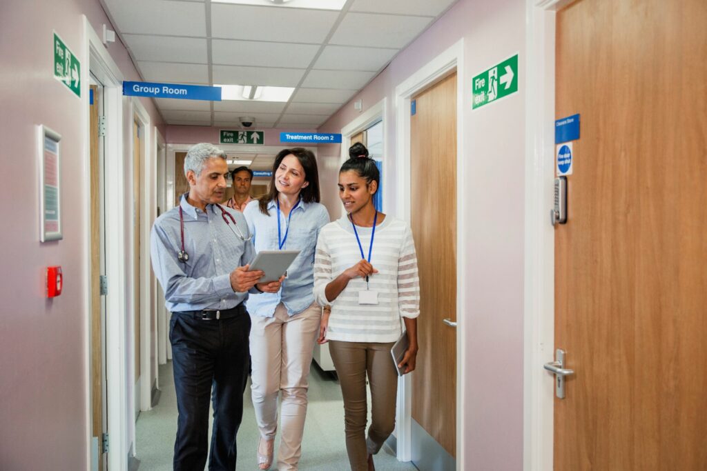Three doctors walking down corridor discussing data on a tablet computer