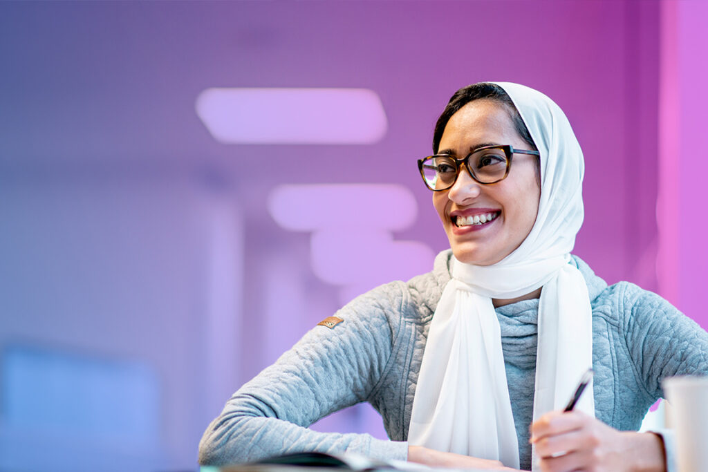 Smiling young woman wearing white headscarf against pink/purple background