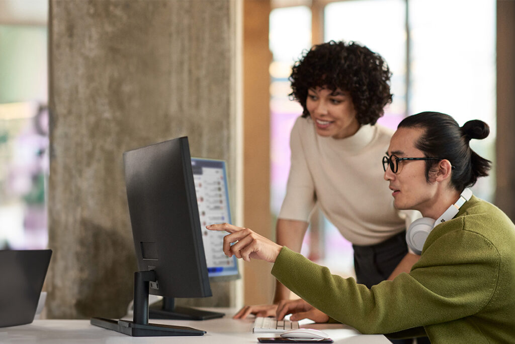 Male and female colleagues collaborating around desktop computer in modern-looking office