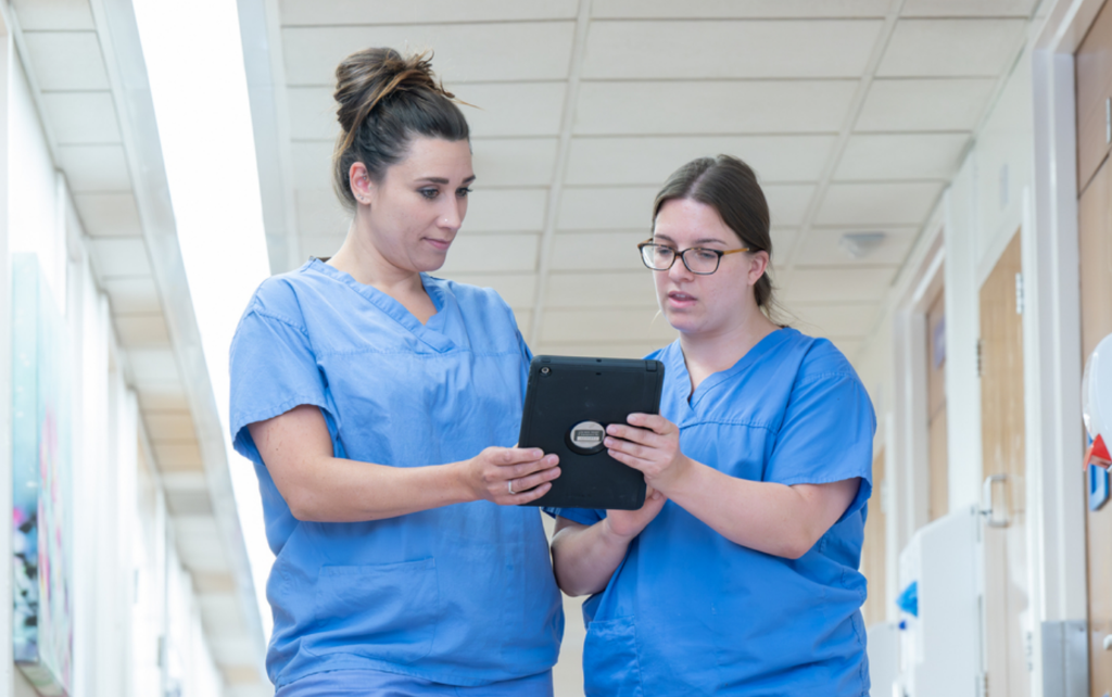 Two midwives discussing work while looking at a tablet computer in hospital