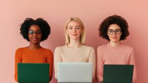 Three young women looking at the camera with laptops in front of them