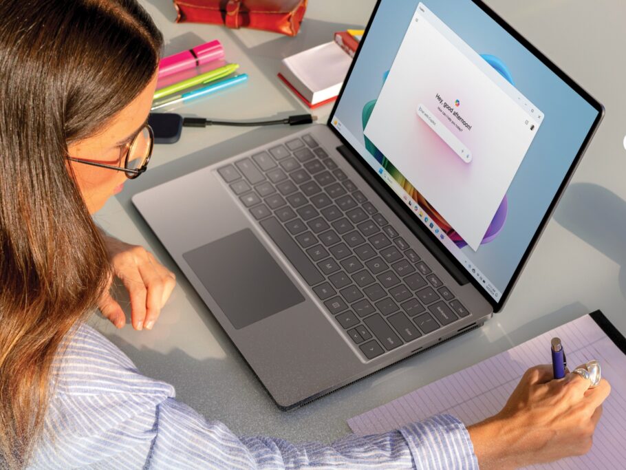 Young woman writing on pad with laptop showing Copilot on screen