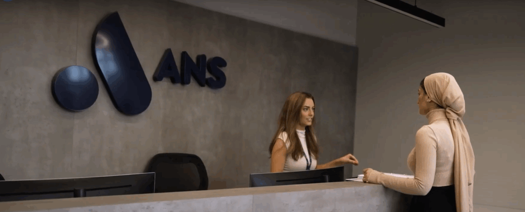 ANS logo behind receptionist talking to colleague