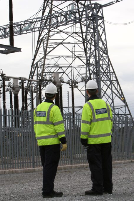 Two UK Power Networks engineers inspecting an electricity pylon and substation