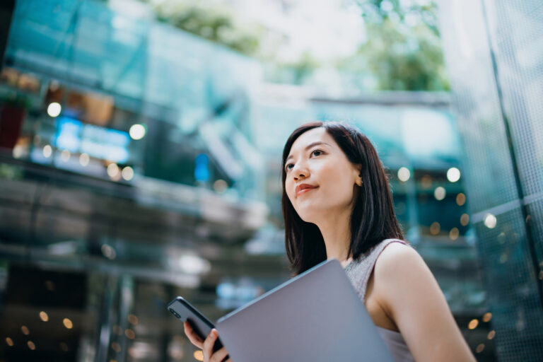 Successful and modern young Asian businesswoman carrying smartphone and laptop symbolising human face of recruitment